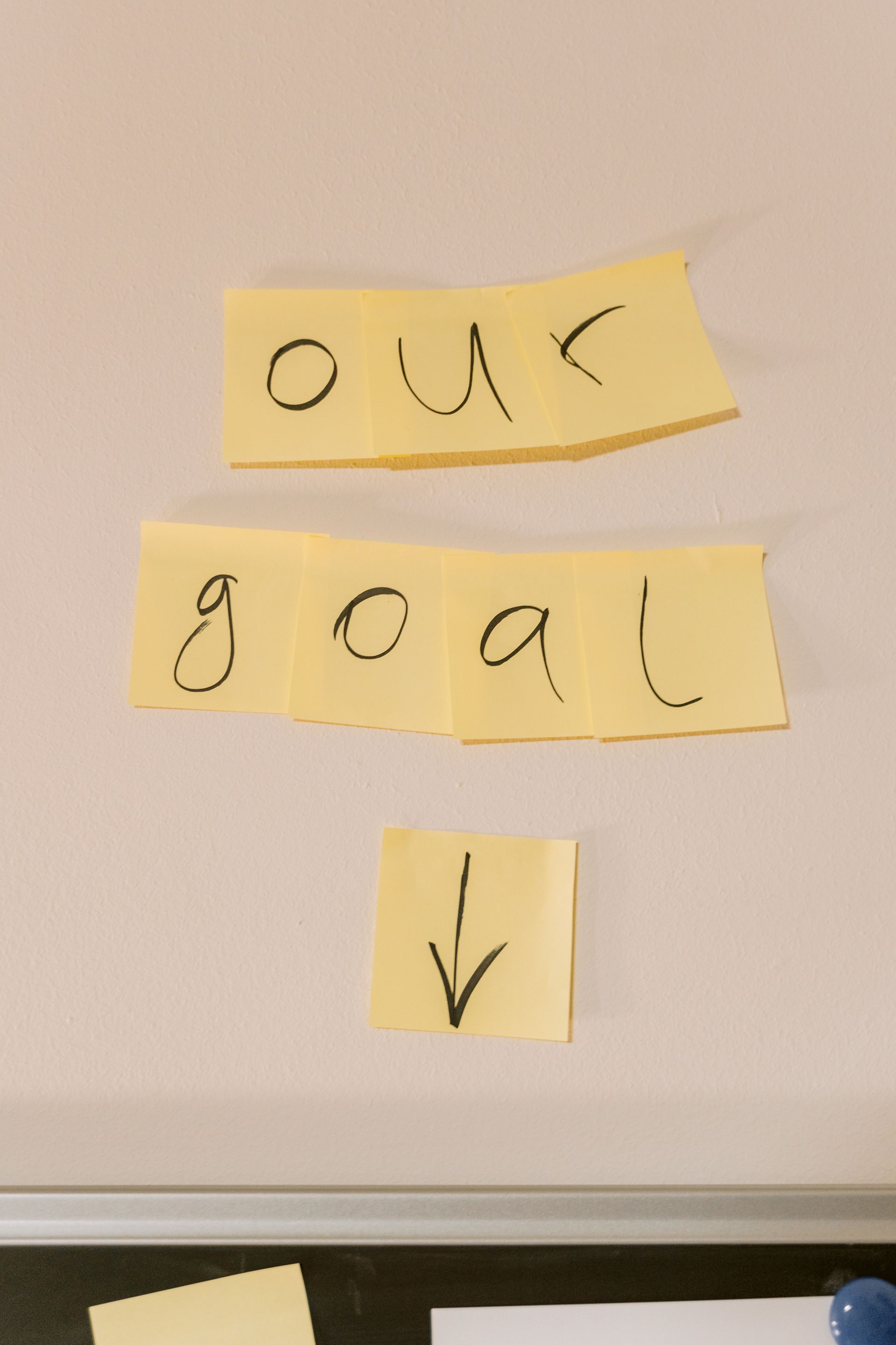 Yellow sticky notes stuck on a wall spelling out the words our goal, above a hand-drawn arrow pointing downward